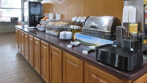 A buffet counter with various food items, a coffee machine, and a refrigerator. - Comfort Inn Port Huron (Port Huron)