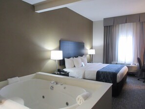 A hotel room with a large bathtub, a bed with a headboard, two bedside lamps, and a window with curtains. - Comfort Inn Port Huron (Port Huron)