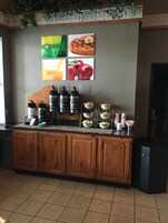 A breakfast bar with coffee dispensers, bowls of food, and a wall with pictures of food and a green sign.