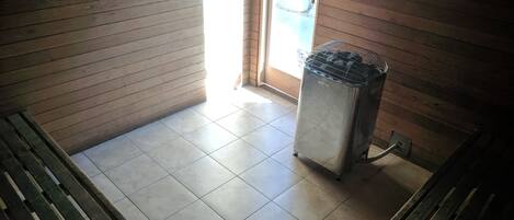 A room with wooden walls, a tiled floor, a bench, and a trash bin.