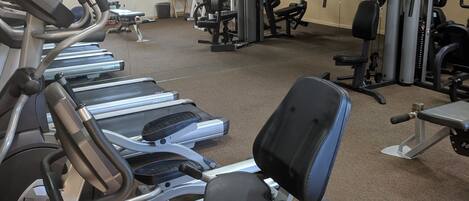 A gym with treadmills, a rowing machine, and weightlifting equipment.