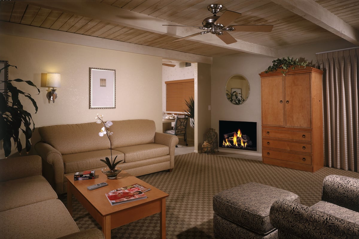A cozy living room with a sofa, armchairs, a coffee table, a fireplace, and a ceiling fan.