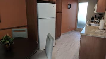 A compact kitchen with wooden cabinets, a white refrigerator, a clock on the wall, and a dining area with a table and chairs.