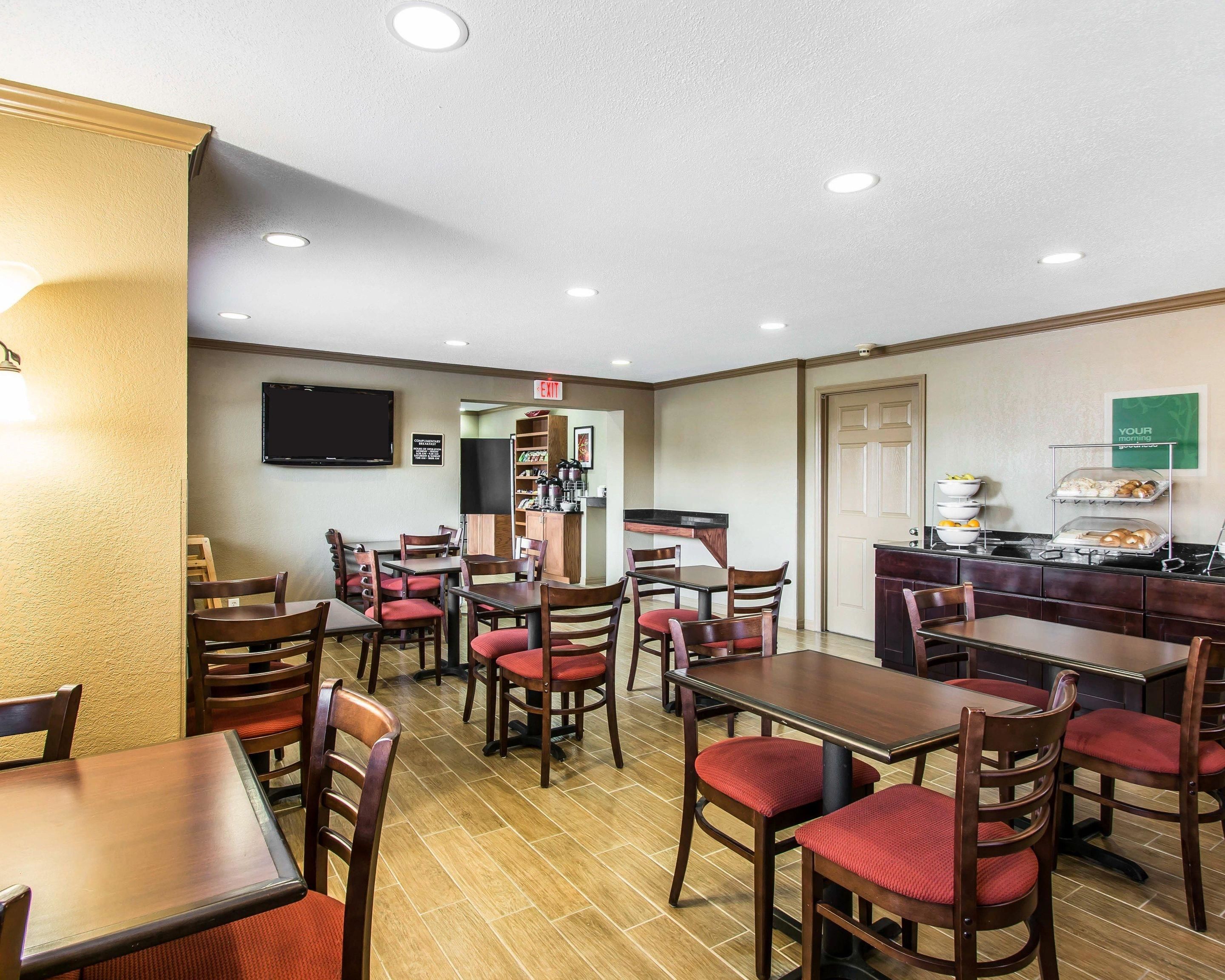 A hotel dining area with multiple tables and chairs, a kitchen area, and an exit sign.