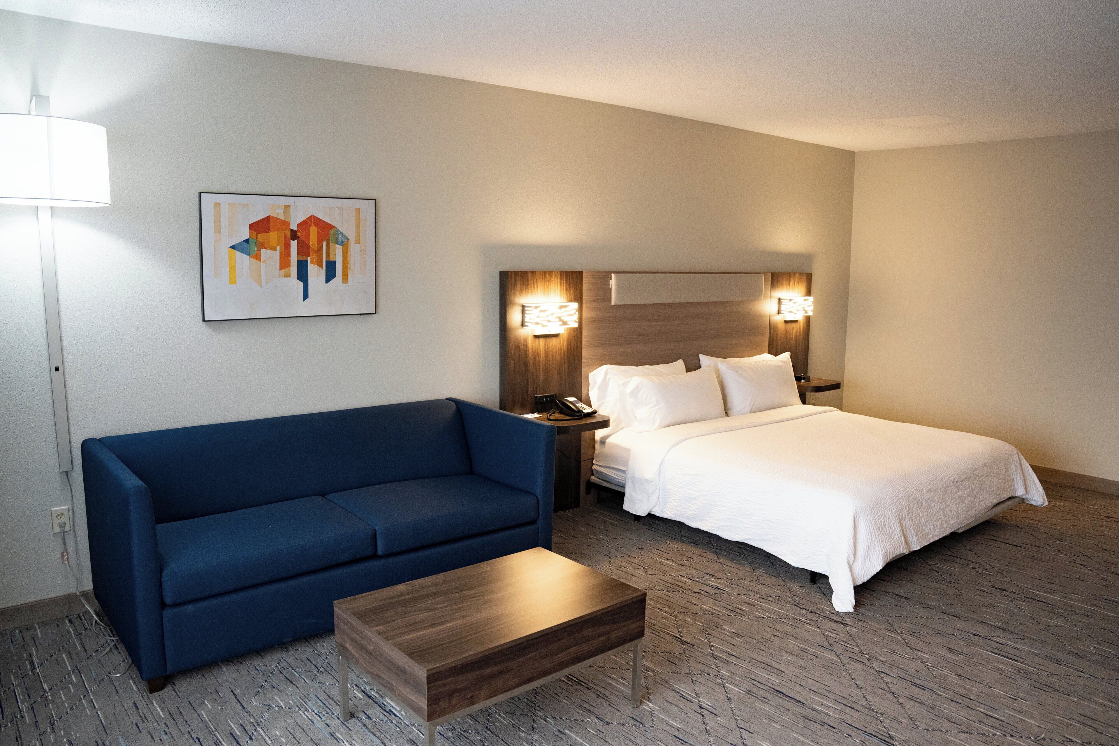 A hotel room with a bed, a blue sofa, a wooden coffee table, and a painting on the wall.