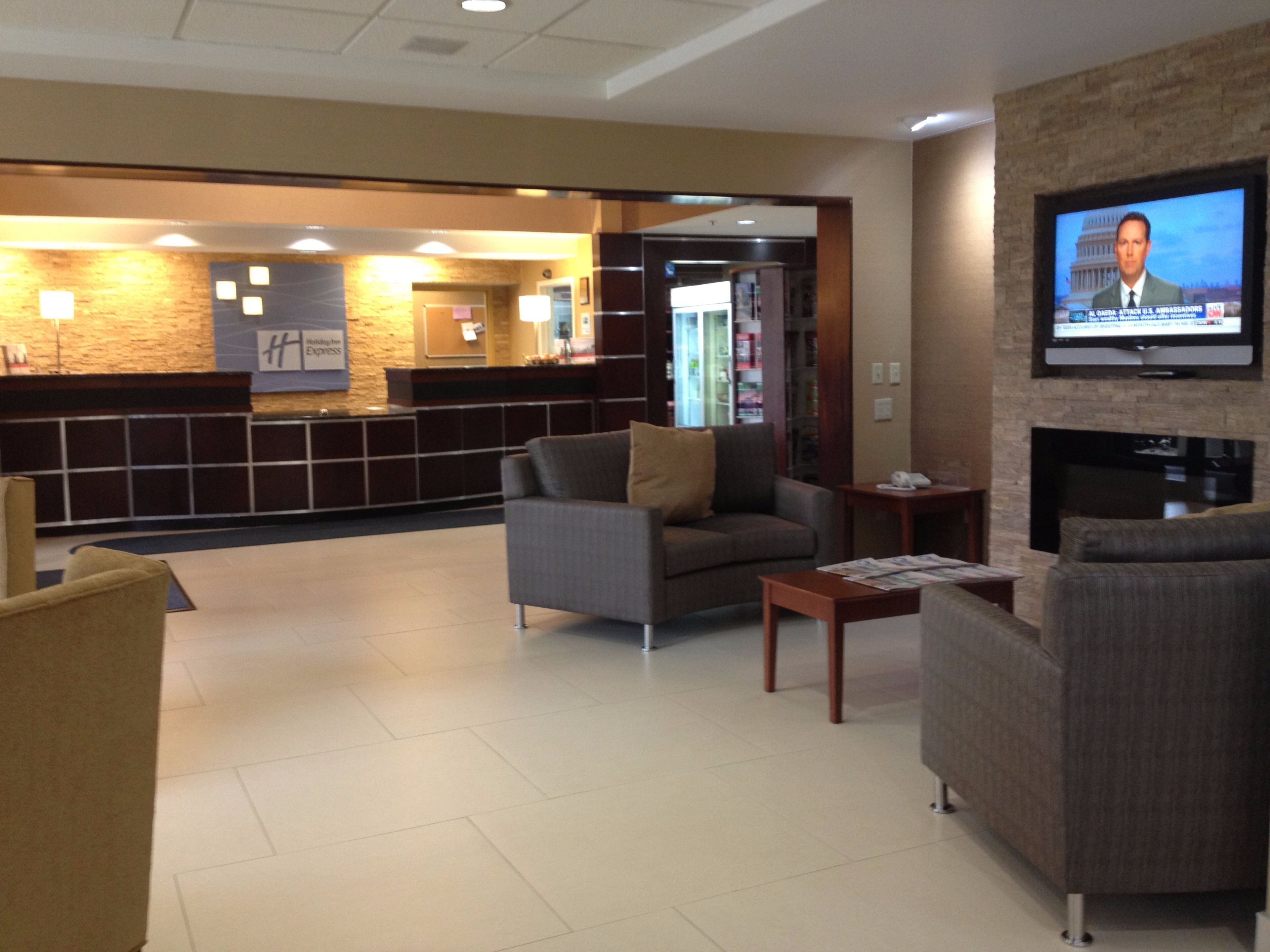A hotel lobby with a reception desk, seating area, and a television displaying news.