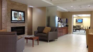 A hotel lobby with a fireplace, seating area, and a dining area.