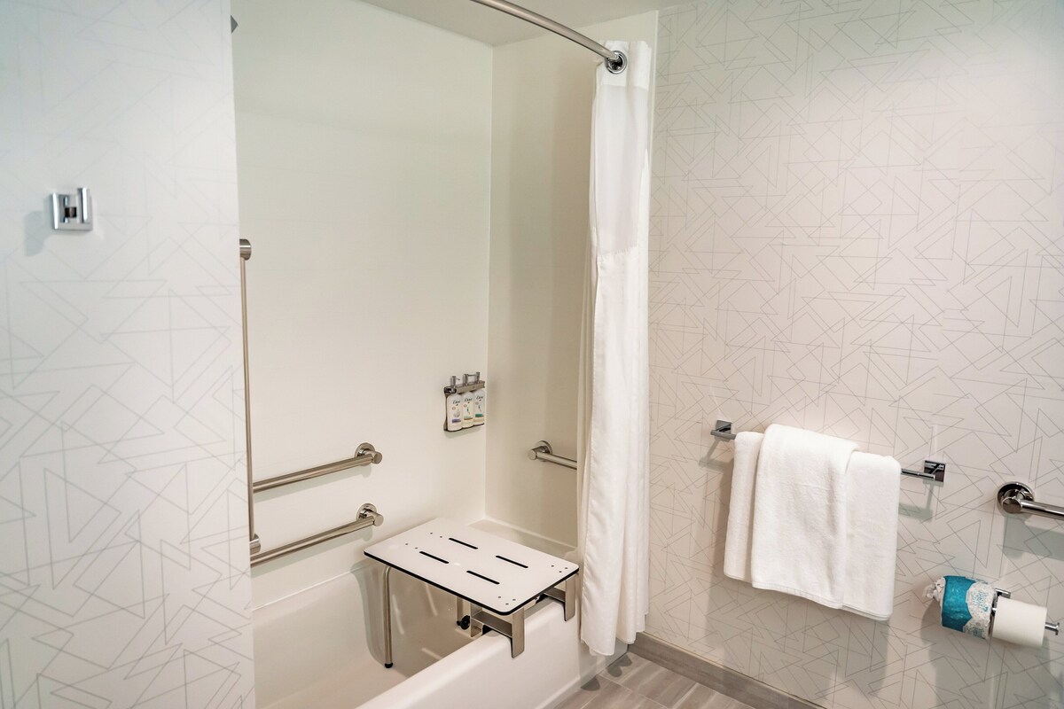 Uma casa de banho moderna com cabine de duche em vidro, um porta-toalhas branco e um rolo de papel higiénico.