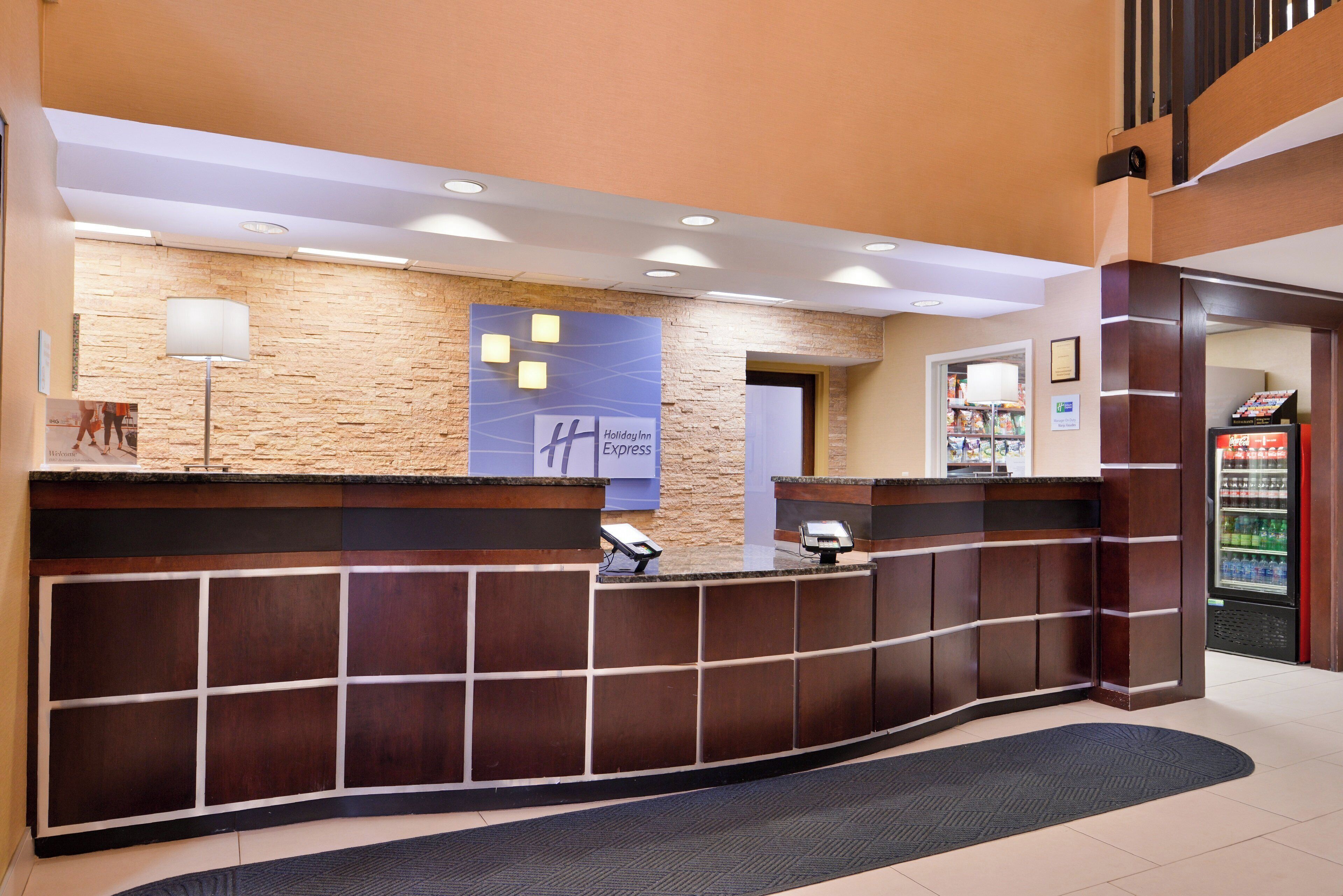 A hotel reception desk with a stone wall backdrop, a digital kiosk, and a vending machine.