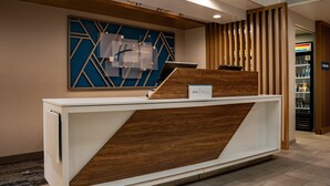 A reception desk with a modern design, a blue geometric wall art piece, and a wooden panel. - Holiday Inn Express Hotel & Suites West Chester by IHG (West Chester)