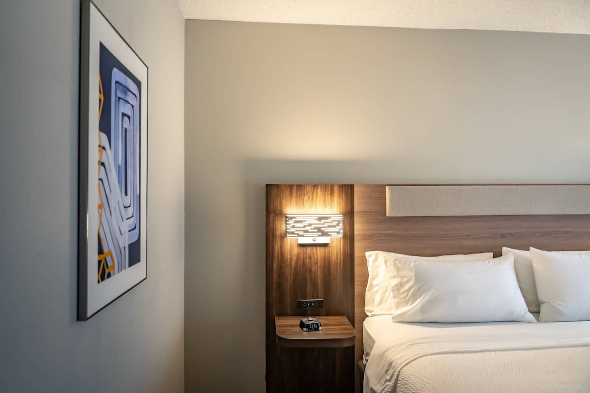 A hotel room with a bed, a nightstand, a wall-mounted light, and a framed picture.