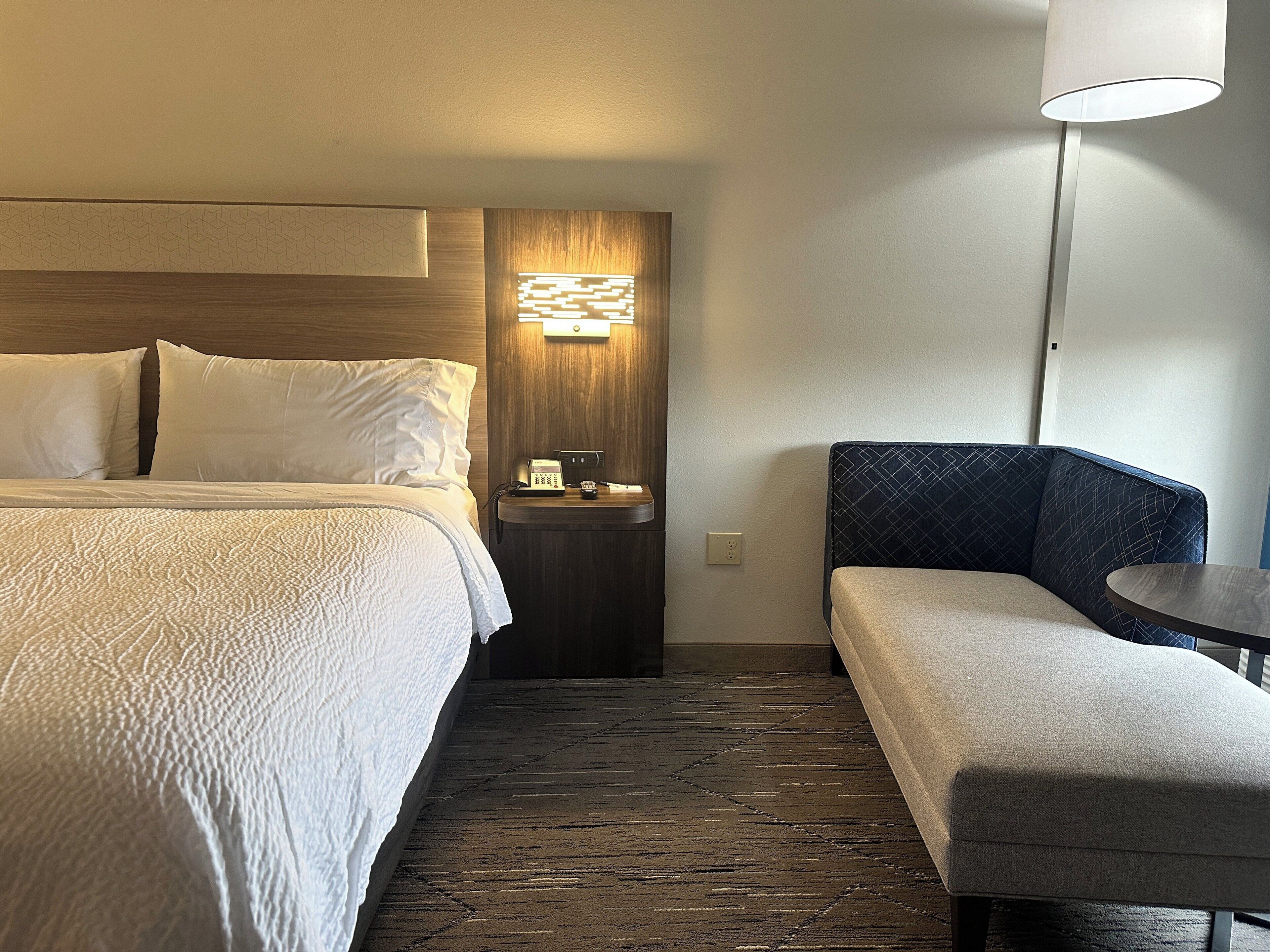 A hotel room with a bed, bedside table, lamp, and a seating area.