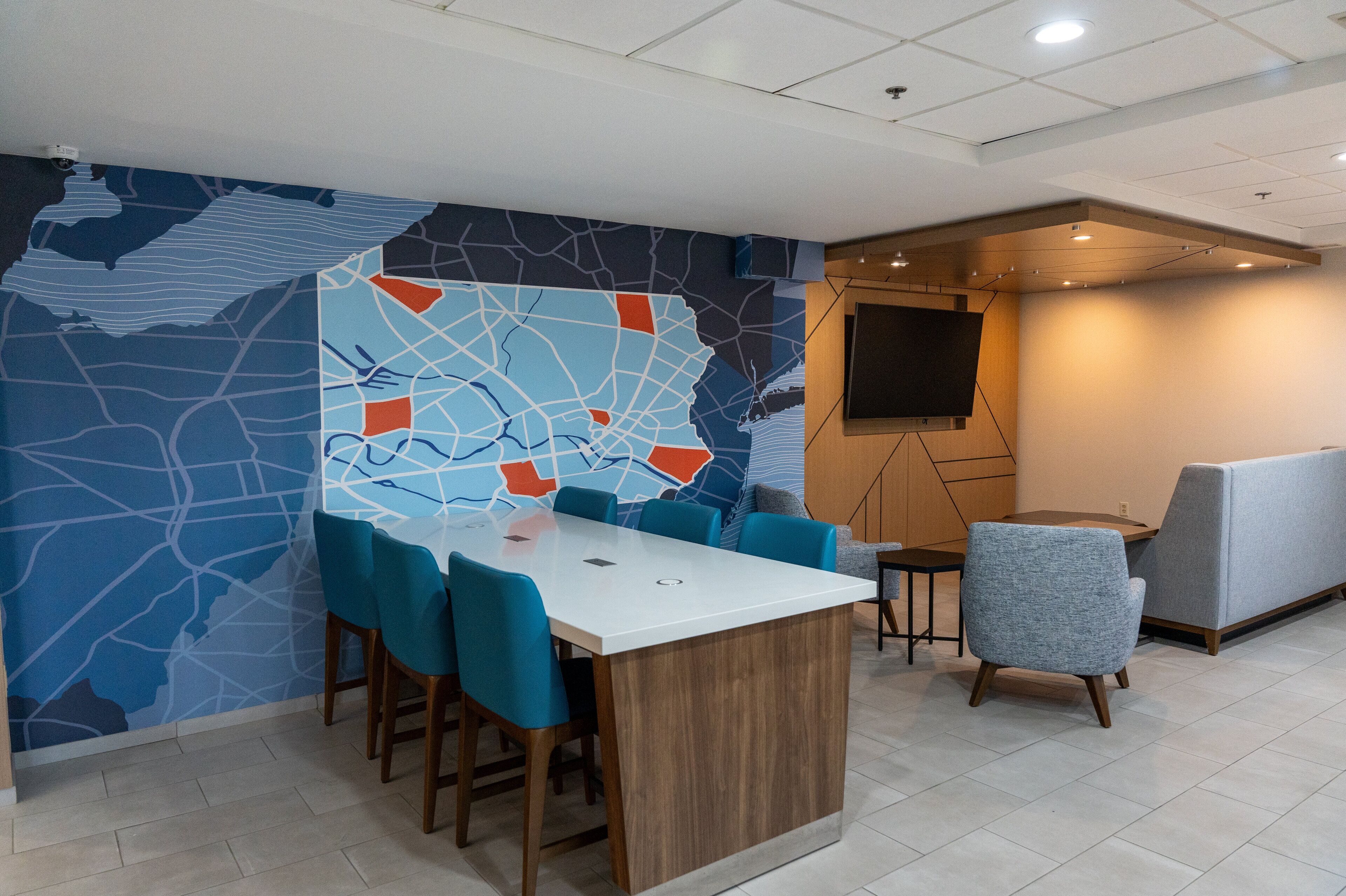 Un espacio de oficina moderno con un gran mural de mapa, una mesa de conferencias blanca, sillas color aguamarina y un sofá gris.
