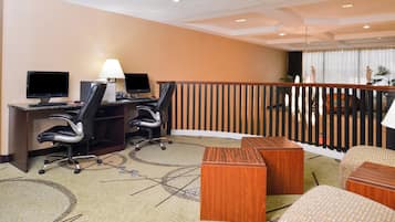 A hotel room with a desk, two monitors, a lamp, a chair, a small table, and a view of the balcony.