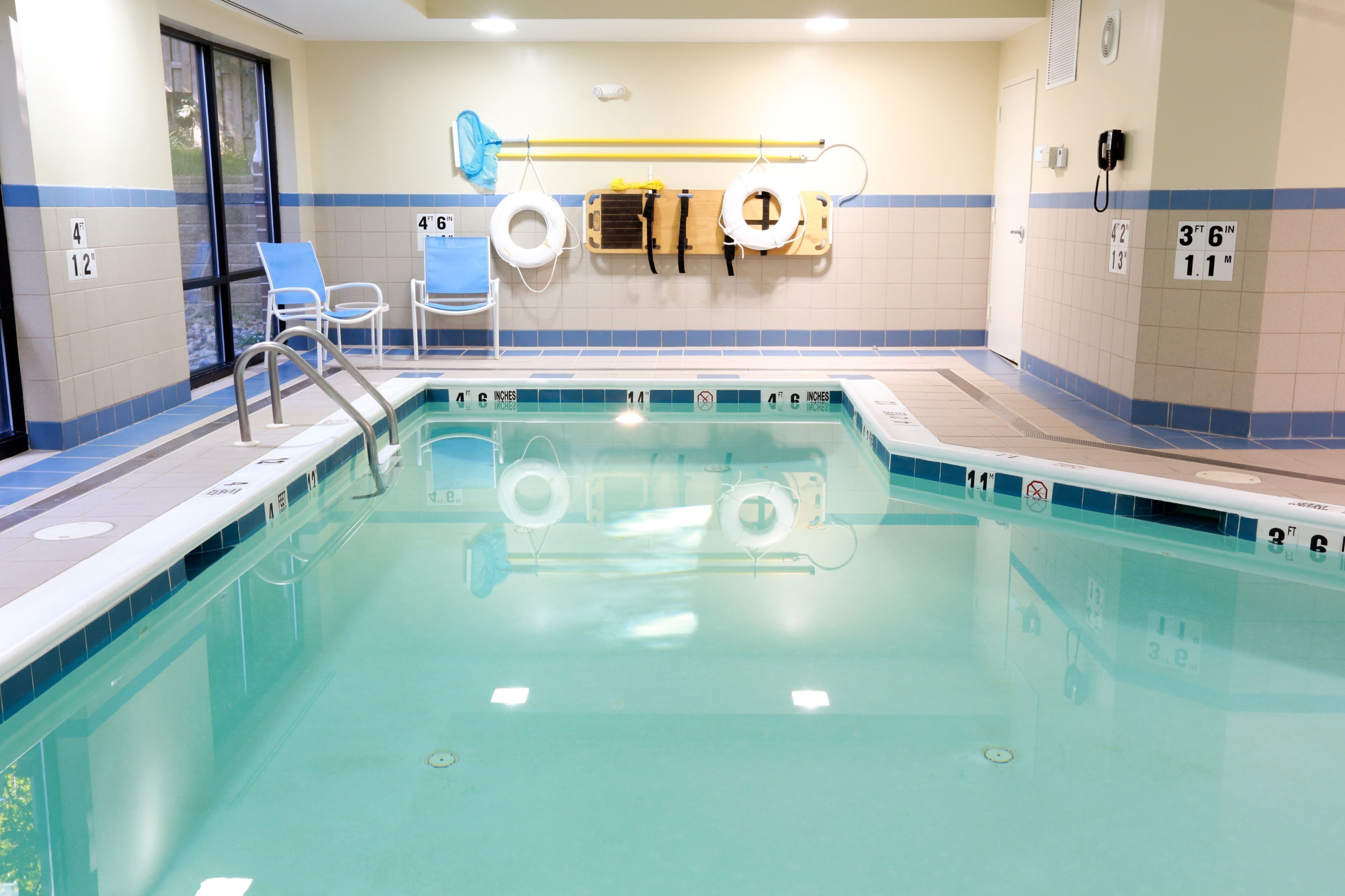 A swimming pool with a ladder, lifebuoys, and a changing room with blue chairs.