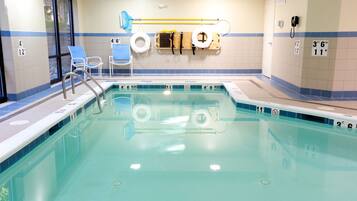 A swimming pool with a ladder, lifebuoys, and a changing room with blue chairs.