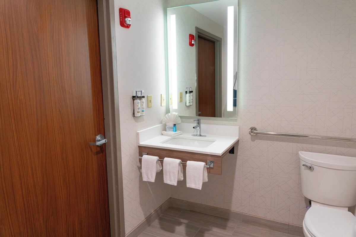 Um banheiro moderno com porta de madeira, pia branca, espelho e vaso sanitário.