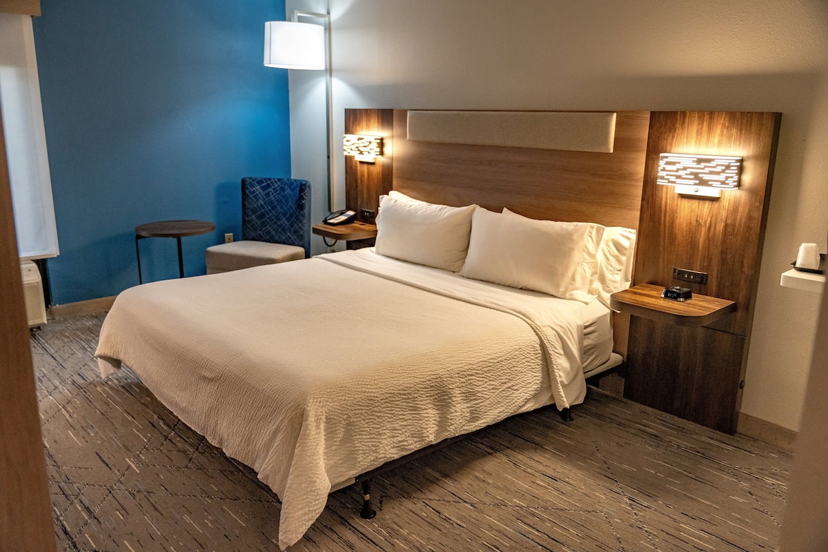 A hotel room with a large bed, a bedside table with a lamp, and a small chair.