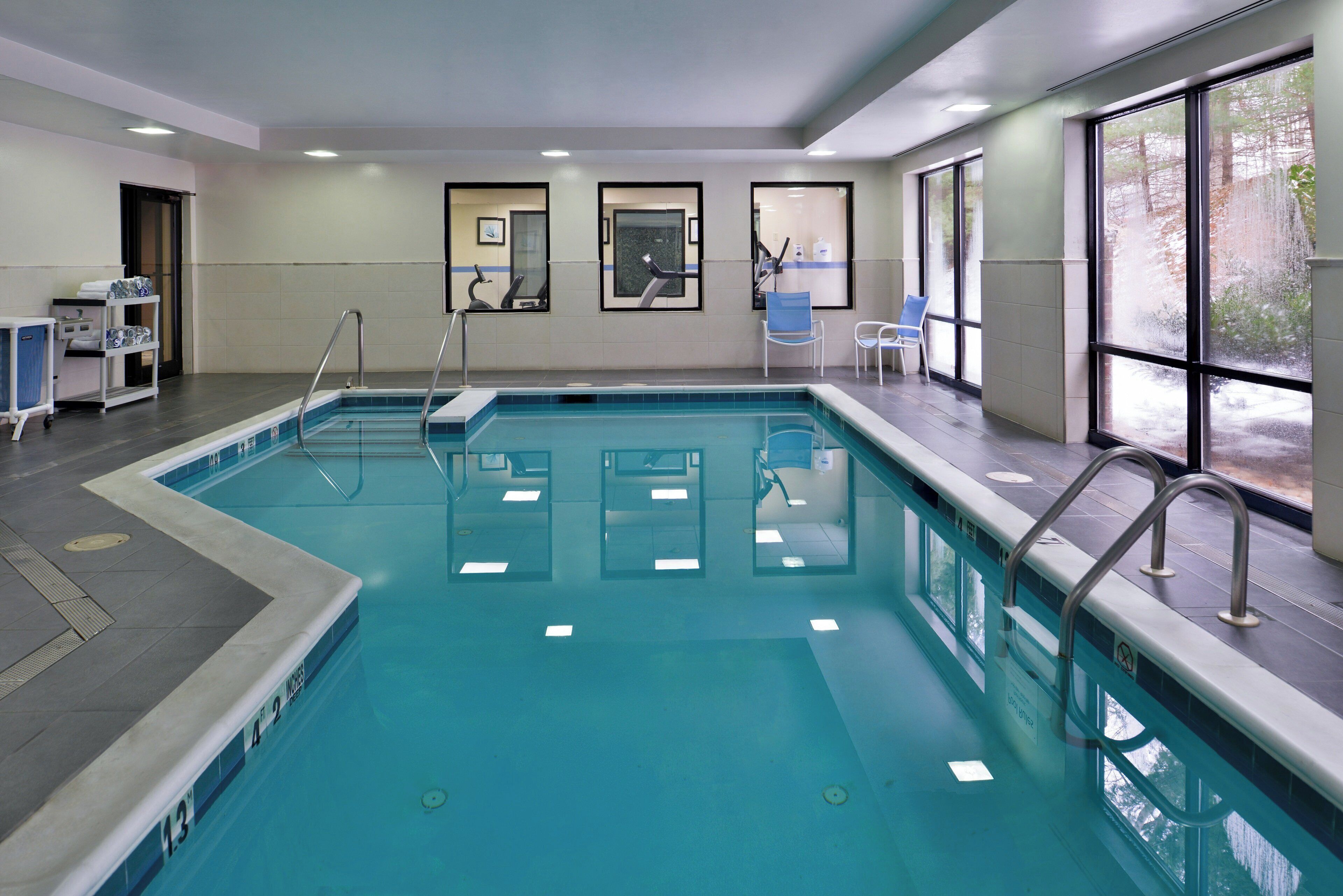 A swimming pool with a clear water surface, surrounded by a tiled deck, and equipped with safety railings.