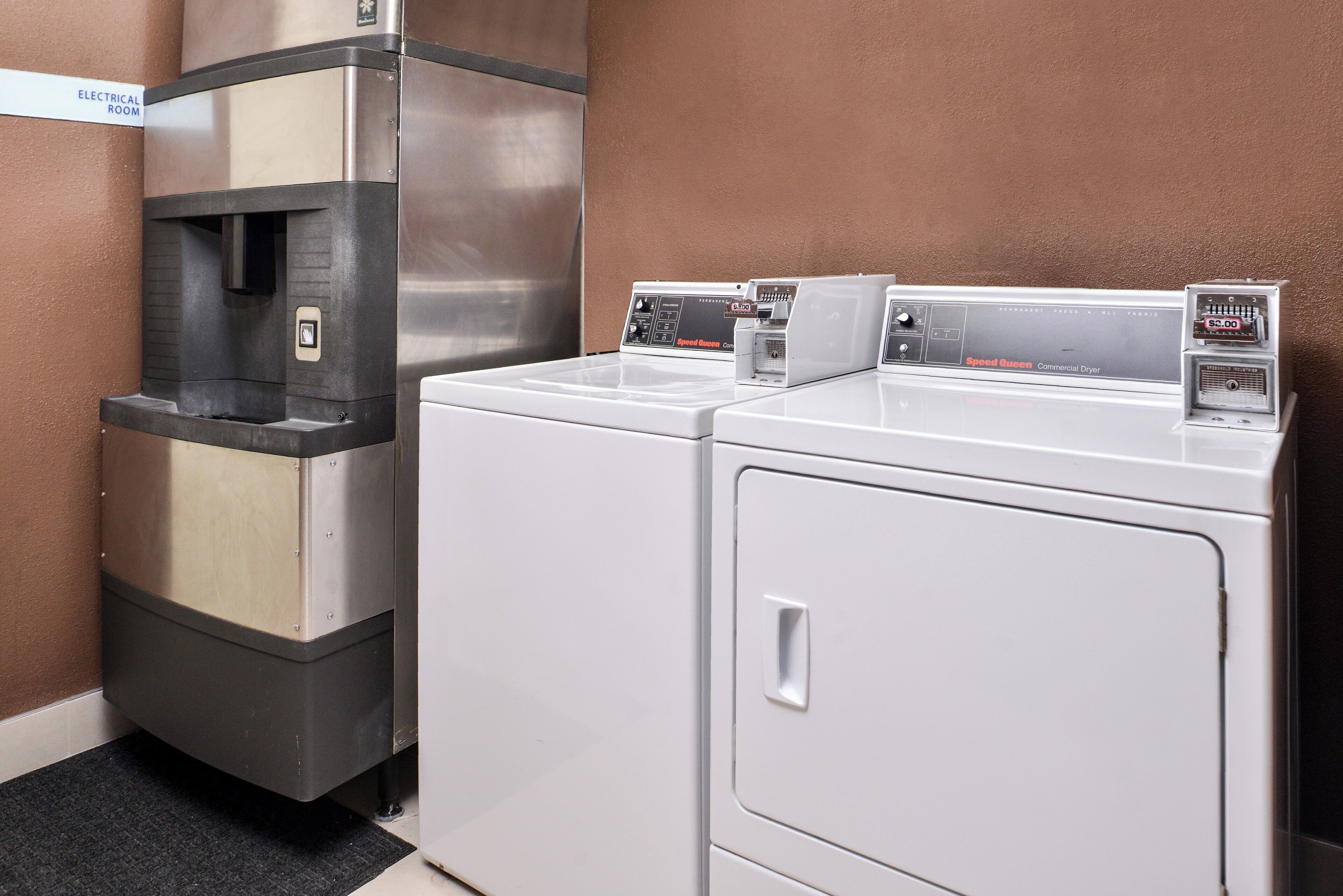 A laundry area with two white washers and a stainless steel dryer, a water fountain, and a sign indicating the room is for electrical use.