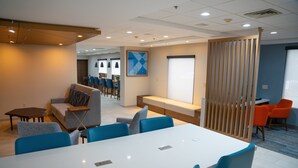 A modern conference room with a white table and blue chairs, a sofa, and a wooden partition. - Holiday Inn Express Hotel & Suites West Chester by IHG (West Chester)