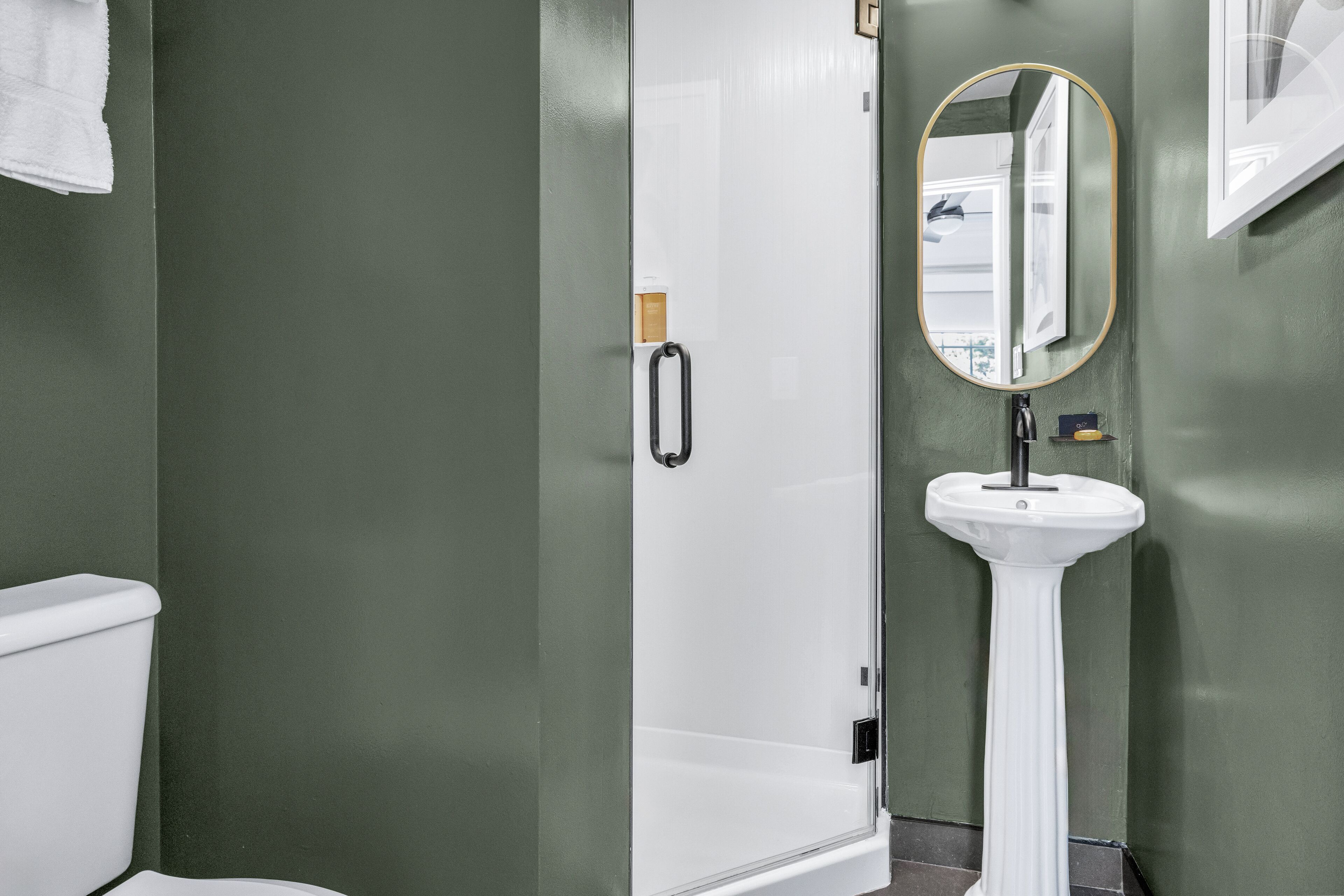 Un baño con inodoro blanco, lavamanos pedestal blanco y cabina de ducha de vidrio.