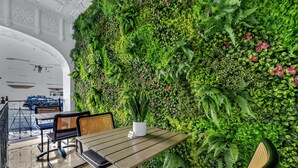 A dining area with a table and chairs, a potted plant, and a green wall with foliage and flowers.