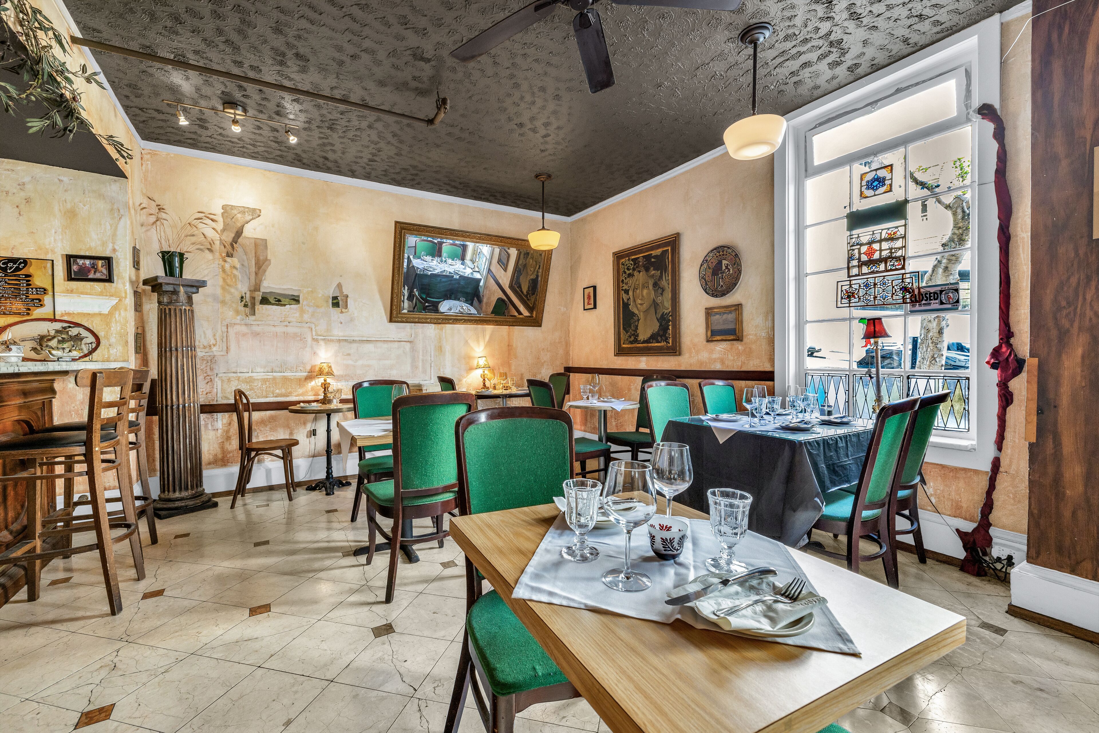 Comedor con varias mesas y sillas, un ventilador de techo y un ventanal con vistas.