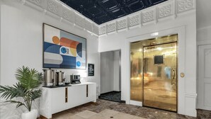 A lobby with a reception desk, a large abstract painting, a potted plant, a gold elevator, and a marble floor.