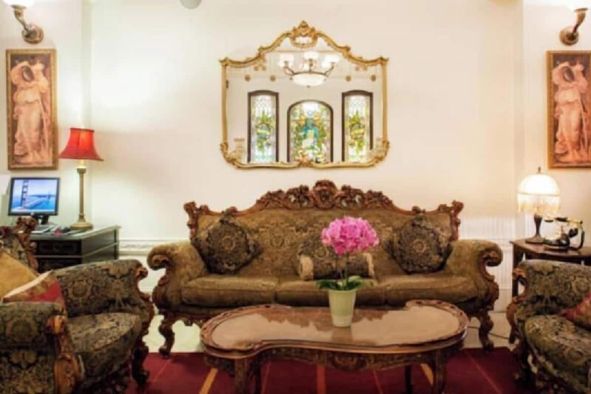 A room with a large ornate sofa, matching armchairs, a glass coffee table, and a decorative mirror above the sofa.
