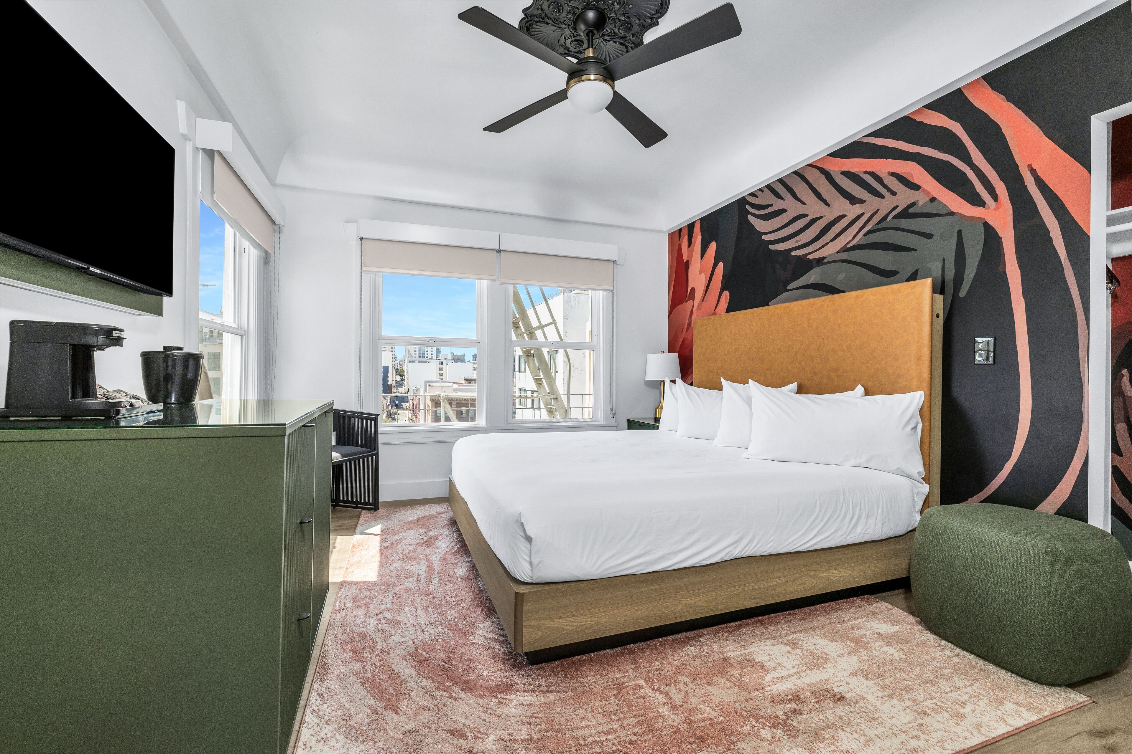 A hotel room with a bed, a green cabinet, a flat-screen TV, and a city view through the window.
