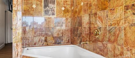 A modern bathroom with a marble tile wall, a bathtub, and a framed picture.