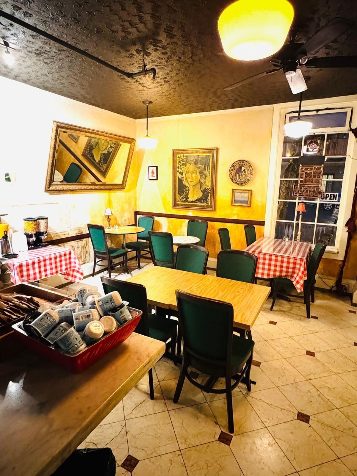 A restaurant interior with tables and chairs, a counter with food items, and artwork on the walls.