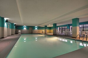 An indoor swimming pool with clear water, surrounded by walls with teal and beige colors, and a seating area with white chairs.