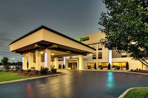 Een Holiday Inn Express hotel met een overdekte ingang, een parkeerplaats en een goed verlichte gevel.