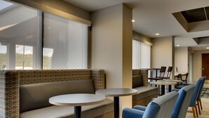 A modern hotel lobby with a seating area featuring a sofa and round tables, large windows, and a view of the outdoors. - Holiday Inn Express Horse Cave by IHG (Horse Cave)