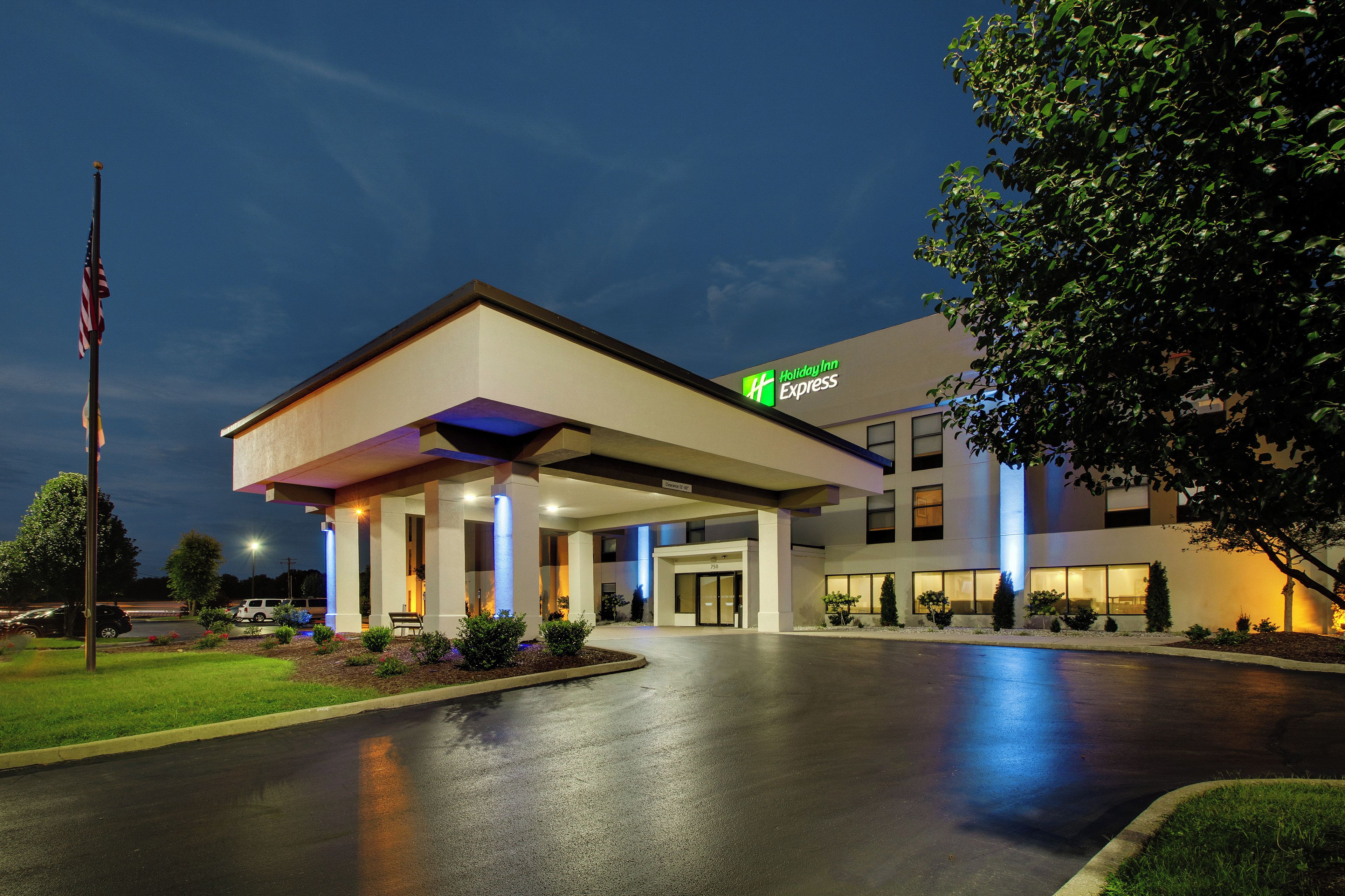 Edificio de Holiday Inn Express con entrada cubierta, una bandera y fachada bien iluminada.