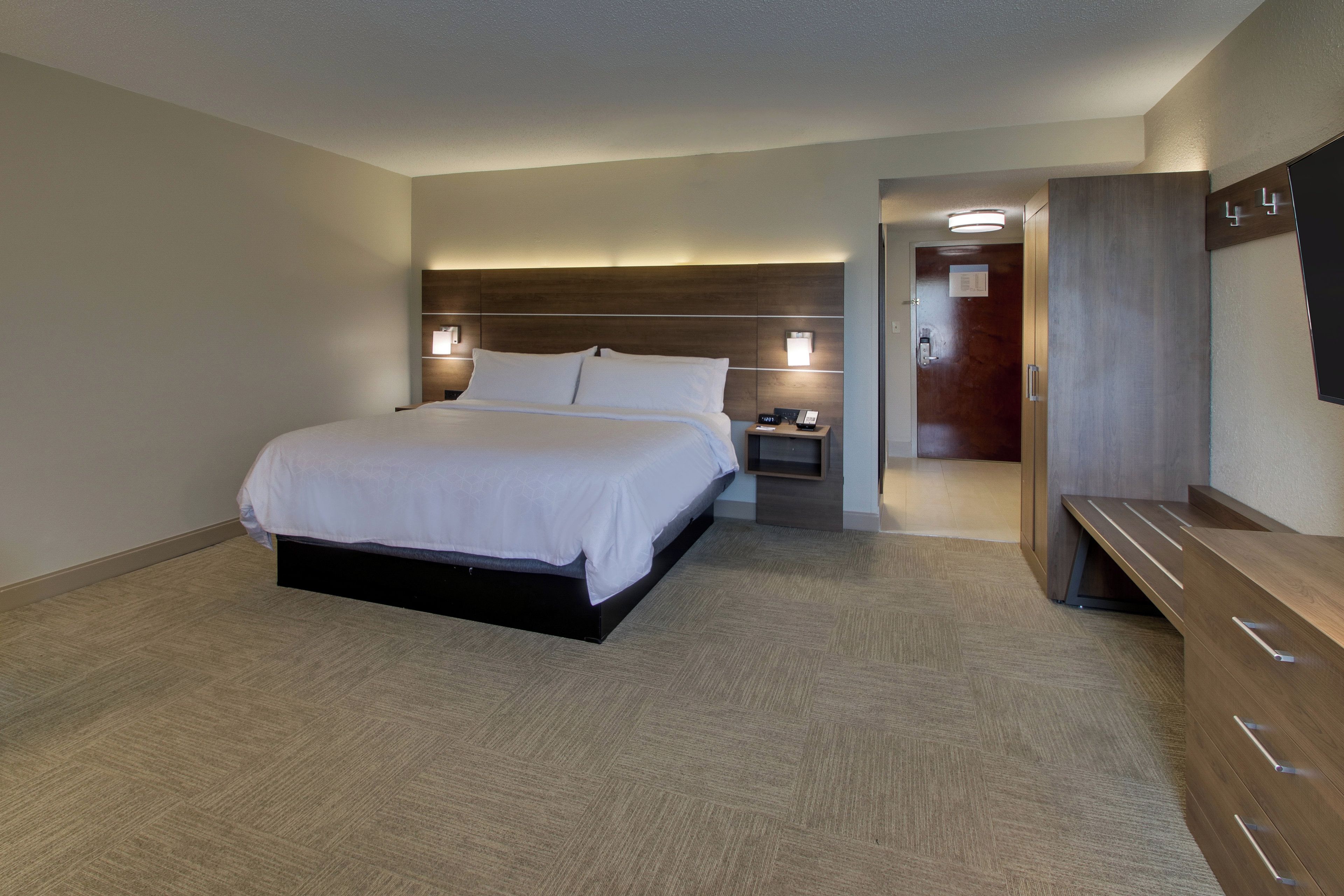 Una habitación de hotel con una cama grande, mesitas de noche, un escritorio y un armario.