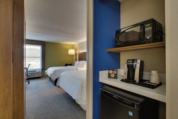 A hotel room with two beds, a microwave, a coffee maker, and a small refrigerator.