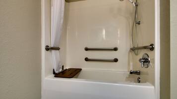Una bañera con cabezal de ducha, barras de apoyo y una bandeja de madera.