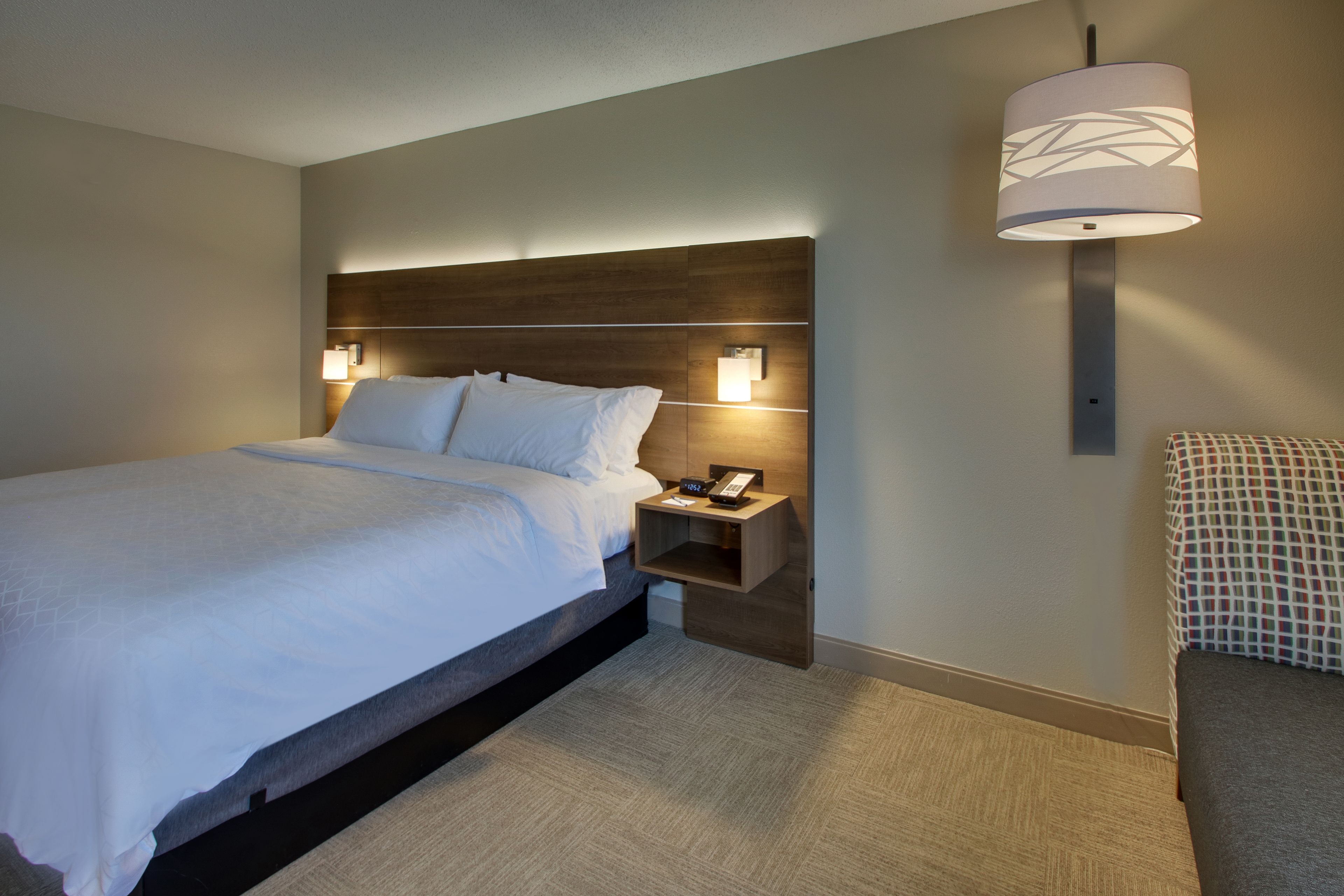 Ett modernt hotellrum med en stor säng, sänglampor, ett nattduksbord och en väggmonterad lampa.
