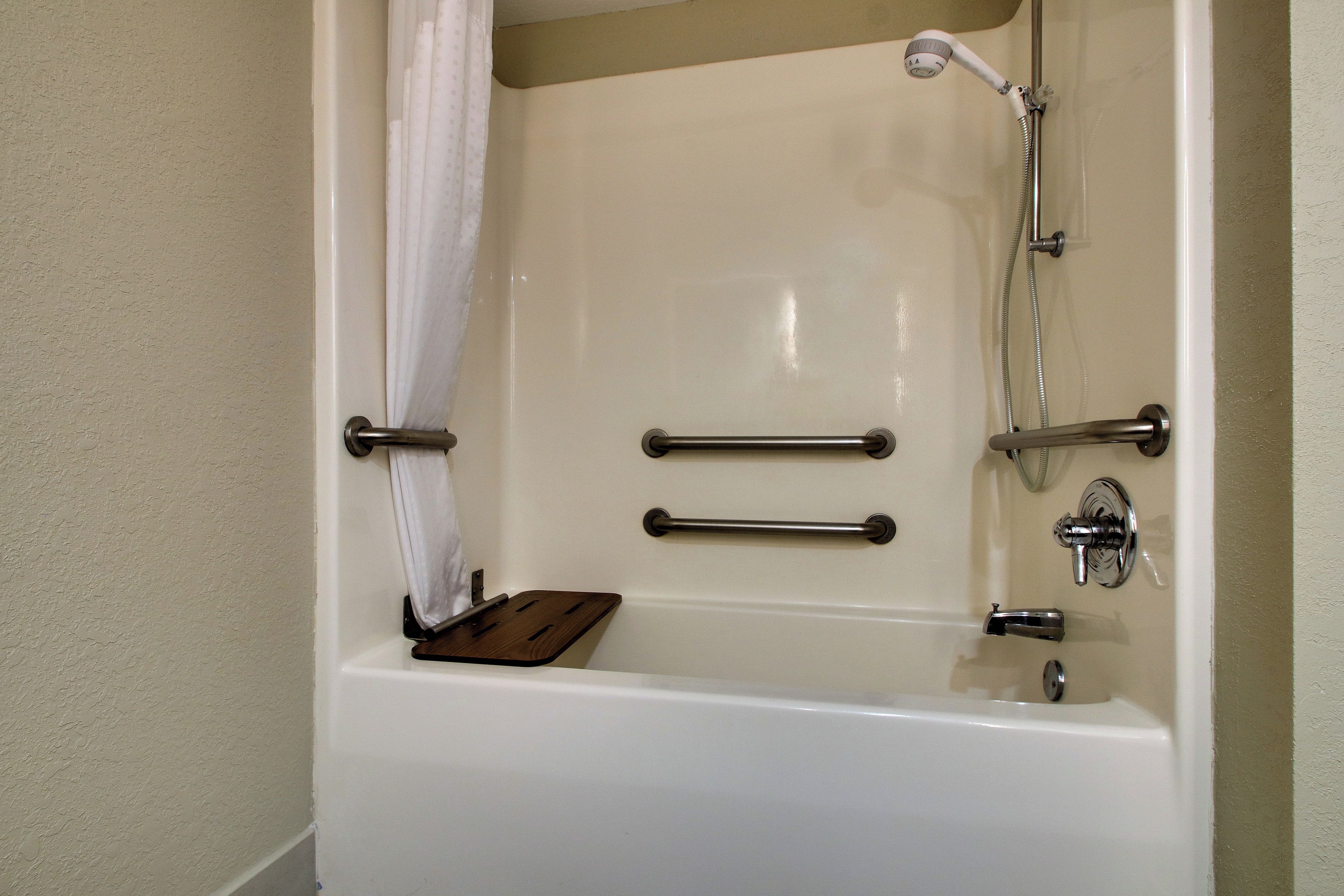 Una bañera con ducha, barras de apoyo y un estante de madera.