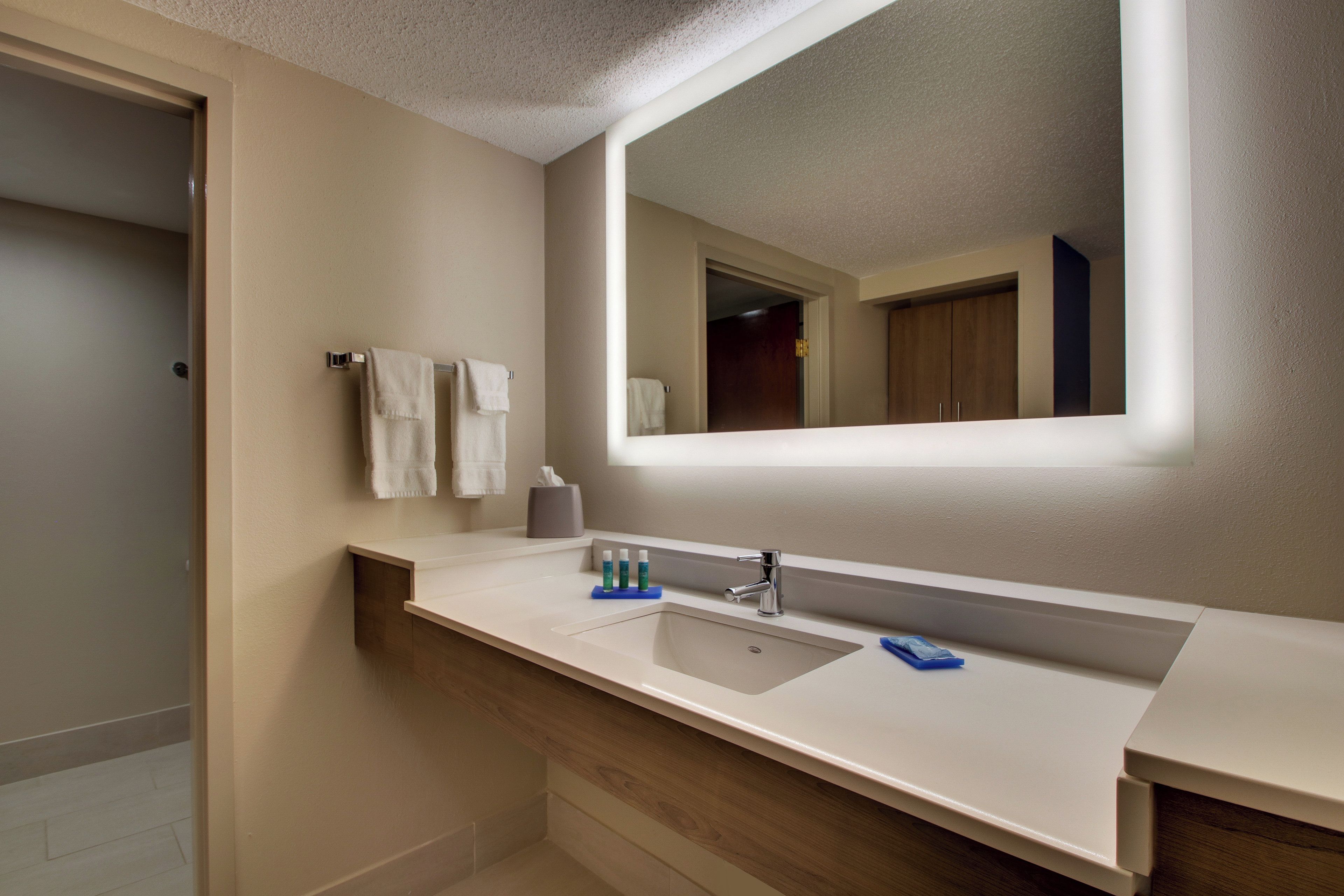 Un baño moderno con un espejo grande, un lavamanos y dos toallas colgadas en un perchero.