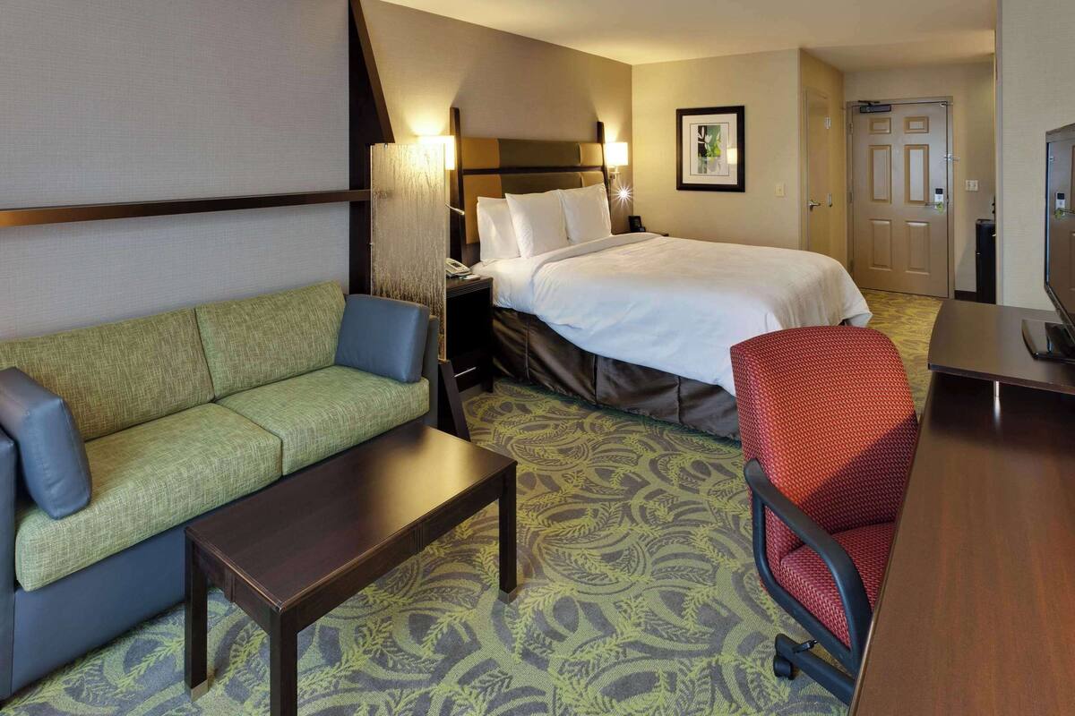 A hotel room with a bed, a sofa, a chair, a desk, and a nightstand.
