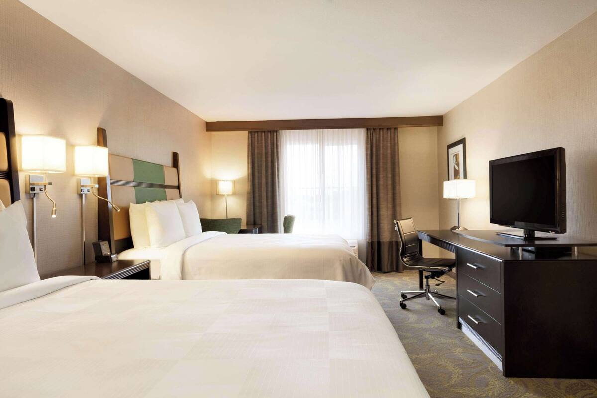 A hotel room with two beds, a desk, a television, and a chair.