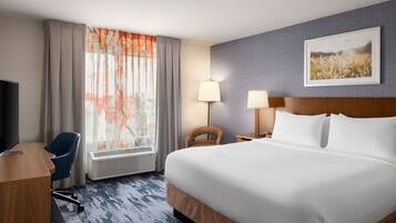 A hotel room with a large bed, a desk, a chair, a TV, a lamp, and a window with curtains.