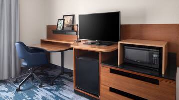 Habitación de hotel con escritorio de madera, computadora, microondas, refrigerador pequeño y una silla azul.