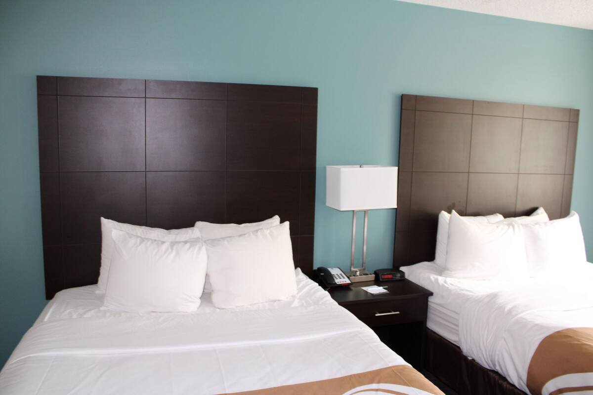 A hotel room with two beds, a nightstand with a lamp, and a telephone.