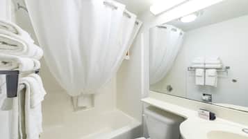 Un baño con bañera, inodoro y lavamanos. Toallas apiladas en un perchero y un espejo sobre el lavamanos.