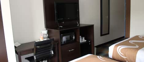 A hotel room with a desk, a television, a microwave, a mirror, and two beds with patterned bedding.